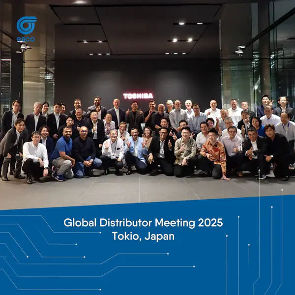 Gruppenfoto aller internationalen Teilnehmer des Toshiba Global Distributor Meeting 2025 vor dem Haupteingang des Toshiba Headquarters in Kawasaki, Tokio. Die Teilnehmer stehen und knien lächelnd vor dem leuchtenden Toshiba-Logo.